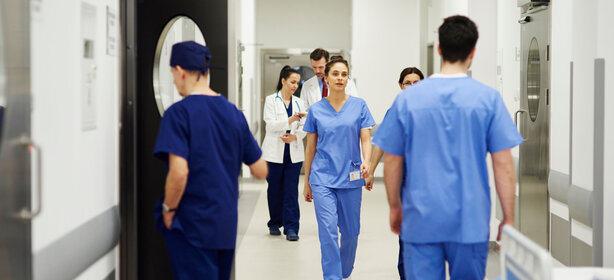 Mehrere Mitarbeitende in blauer Arbeitskleidung gehen durch einen hellen Klinikflur