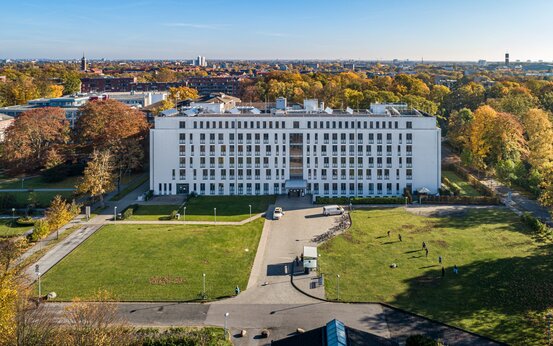 Luftaufnahme eines modernen, weißen Klinikgebäudes mit Flachdach, umgeben von Parkanlagen und Stadtlandschaft
