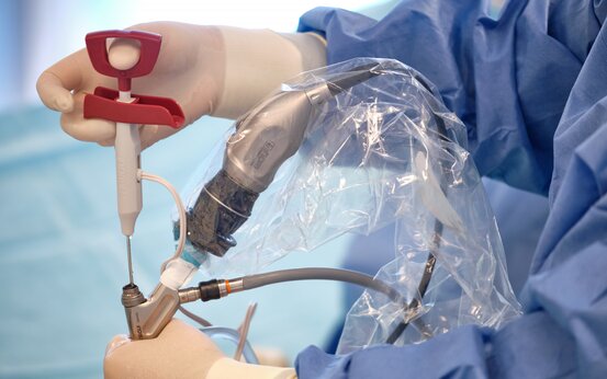 Steril bekleidete Hände von Fachpersonal bei endoskopischer Bandscheibenoperation, OP-Instrumente und blaue OP-Kleidung sichtbar