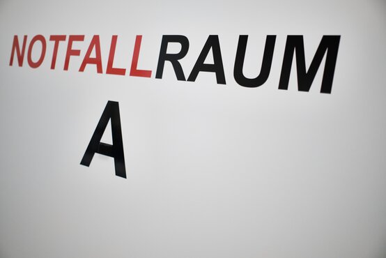 Weiße Wand mit roter und schwarzer Beschriftung „NOTFALLRAUM A“ in der Klinik