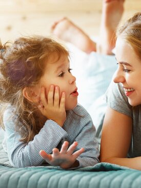 Frau und Kind liegen auf dem Bett und führen ein einfühlsames Gespräch