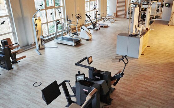 Helles Fitnessstudio mit großen Fenstern, modernen Kraft- und Ausdauergeräten auf Holzfußboden