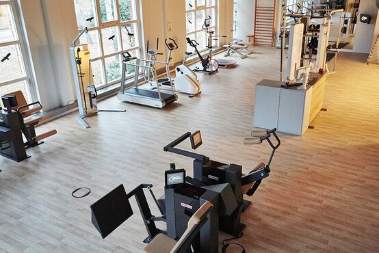 Helles Fitnessstudio mit großen Fenstern, modernen Kraft- und Ausdauergeräten auf Holzfußboden