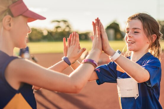 Zwei Mädchen beim Outdoor-Sport klatschen sich lächelnd ab und stehen aufrecht