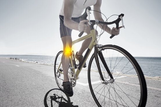 Rennradfahrer auf Küstenstraße, Fokus auf hervorgehobenes rechtes Kniegelenk mit Röntgenansicht, Meer im Hintergrund