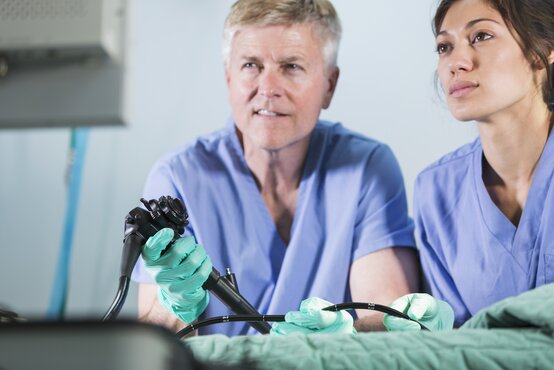 Zwei medizinische Fachkräfte führen Endoskopie durch, Arzt bedient Endoskop, Patient bedeckt im Behandlungsraum