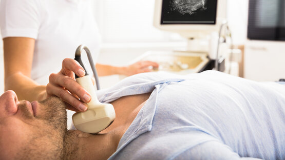 Nahaufnahme einer Ultraschalluntersuchung am Hals eines männlichen Patienten durch eine medizinische Fachkraft in einer modernen Arztpraxis