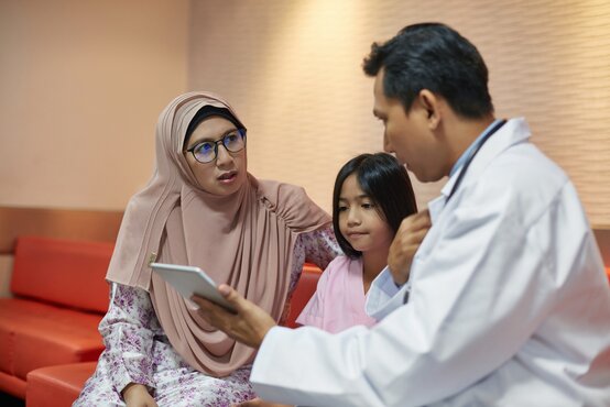 Ärztliches Gespräch mit Frau mit Kopftuch und Kind auf rotem Sofa