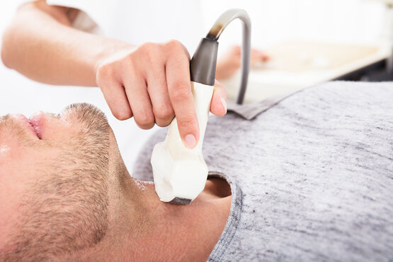 Nahaufnahme einer Schilddrüsenuntersuchung mit Ultraschall am Hals eines liegenden Patienten