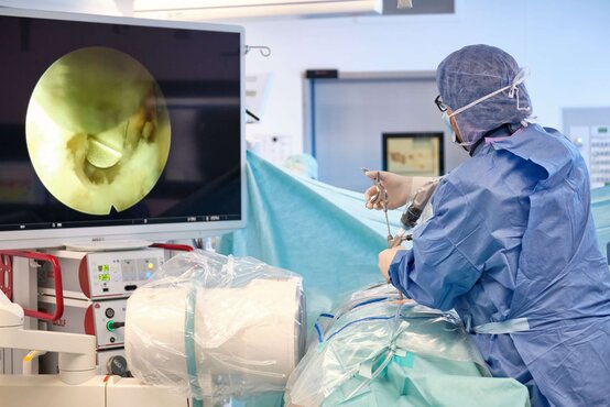 Chirurg in steriler OP-Kleidung führt minimalinvasive Wirbelsäulenoperation durch, Endoskopbild auf großem Monitor
