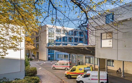 Eingangsbereich einer modernen Notaufnahme mit mehreren Rettungsfahrzeugen und Lieferwagen vor dem Klinikgebäude