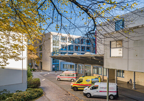 Eingangsbereich einer modernen Notaufnahme mit mehreren Rettungsfahrzeugen und Lieferwagen vor dem Klinikgebäude