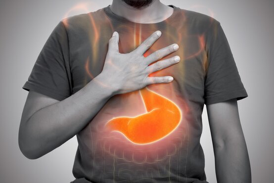 Mann hält sich die Brust, orangefarbene Grafik zeigt brennenden Magen und Speiseröhre als Reflux-Darstellung