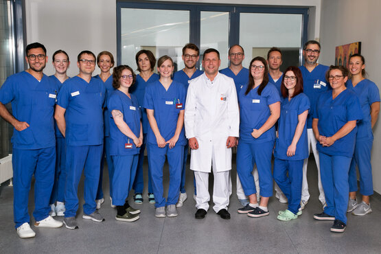 Gruppenfoto des Radiologie-Teams mit 15 Personen in blauer Arbeitskleidung und weißem Arztkittel