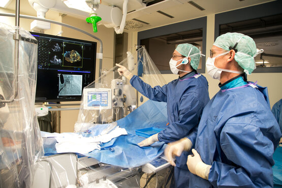 Zwei Ärzte in blauen OP-Kitteln und Schutzmasken betrachten Herzbildgebung am Monitor