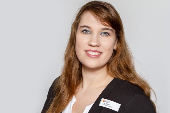 Porträt von Tatjana Riffner im dunklen Blazer vor hellem Hintergrund, lächelt freundlich