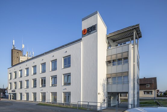 Zugang zur Schön Klinik Lorsch, modernes weißes Klinikgebäude mit großem Logo und mehreren Fenstern bei blauem Himmel