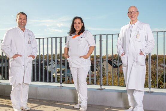 Drei medizinische Fachkräfte in weißer Arbeitskleidung auf Dachterrasse, Team der Wirbelsäulenchirurgie Lorsch