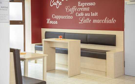 Café-Sitzbereich der Schön Klinik Lorsch mit hellen Holzmöbeln, braunen Polsterbänken und roter Wand