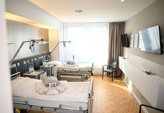 Modernes Patientenzimmer der Schön Klinik Lorsch mit zwei Betten, Holzboden, großem Fenster und neutraler Einrichtung