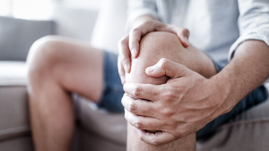 Person hält sich das Knie mit beiden Händen