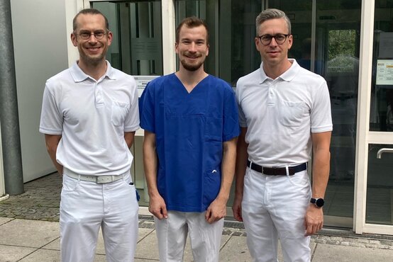 Zwei Ärzte und eine medizinische Fachkraft vor dem Eingang der Schön Klinik München Harlaching