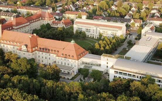 Luftaufnahme der Schön Klinik München Harlaching mit historischen und modernen Gebäuden, roten Dächern und grüner Parklandschaft
