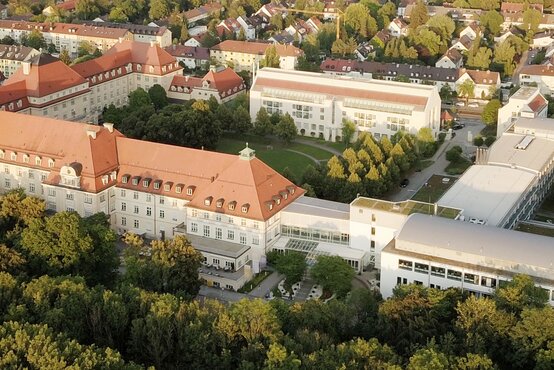 Luftaufnahme der Schön Klinik München Harlaching mit historischen und modernen Gebäuden, roten Dächern und grüner Parklandschaft