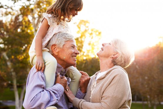 Lächelnde ältere Frau und Mann im Freien, Mann trägt ein junges Mädchen auf den Schultern