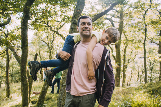 Mann trägt lachendes Kind auf der Schulter, beide im Freien