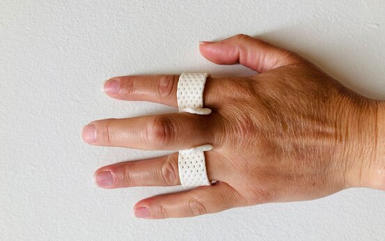 Hand mit zwei weißen, gelochten Fingerschienen an Zeige- und Ringfinger