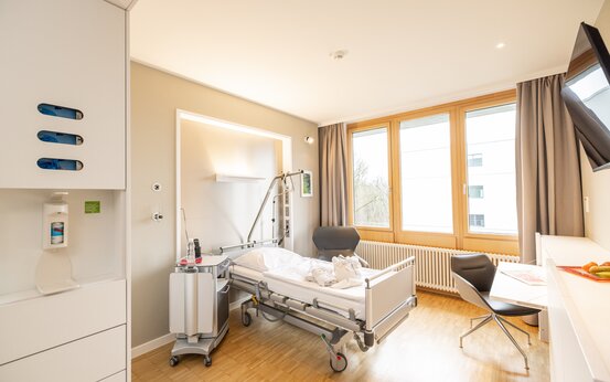 Modernes, helles Einzelzimmer der Schön Klinik mit Pflegebett, Besucherstuhl und großem Fenster