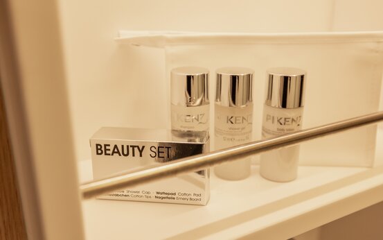 Drei Flaschen Hotel-Kosmetik von PIKENZ und eine silberne Beauty-Set-Box auf weißem Regal im Patientenzimmer