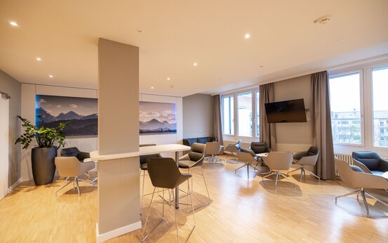 Heller Patienten Aufenthaltsraum mit großen Fenstern, Sitzgruppen und Fernseher