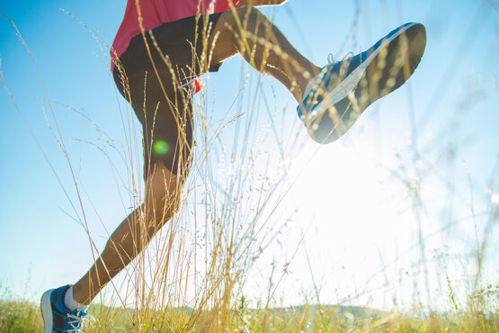 Nahaufnahme laufender Füße auf Wiese bei Sonnenschein, Fokus auf bewegtes, schmerzfreies Sprunggelenk
