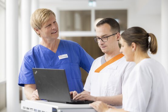 Ärztin und Pflegekräfte besprechen gemeinsam Patientendaten am Laptop