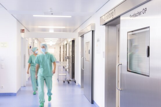 Zwei OP-Mitarbeiter in grüner Kleidung gehen durch den Flur eines modernen Operationsbereichs