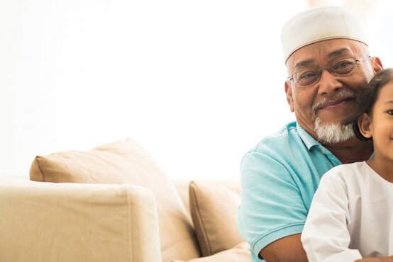 Mann mit traditioneller Kopfbedeckung sitzt mit Kind auf einem Sofa