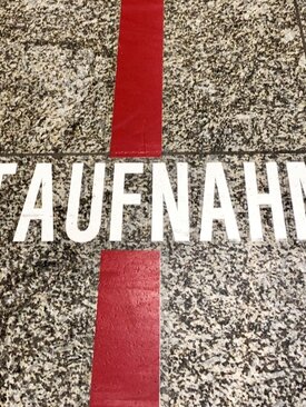 Schriftzug „Notaufnahme“ in weißen Großbuchstaben auf grau-gesprenkeltem Boden, breite rote Linie verläuft senkrecht durch das Wort