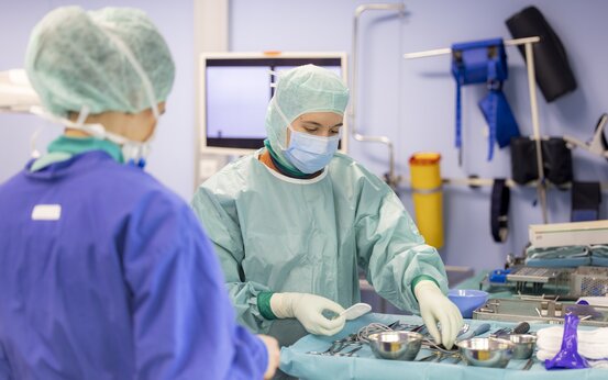 Zwei medizinische Fachkräfte in OP-Kleidung, bereiten chirurgische Instrumente an einem gedeckten OP-Tisch im Operationssaal vor