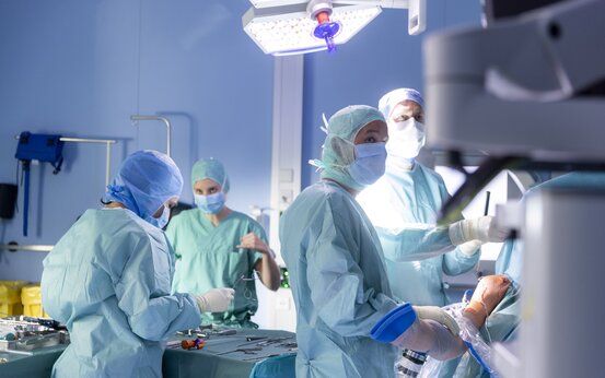 Vier Chirurginnen und Chirurgen in grüner OP-Kleidung operieren einen Patienten im Operationssaal