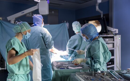 Mehrere Personen in OP-Kleidung und Mundschutz stehen im Operationssaal, OP-Tisch mit chirurgischen Instrumenten