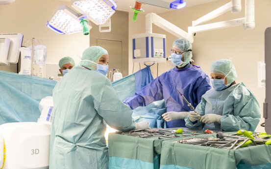 Chirurgisches Team mit Schutzkleidung arbeitet konzentriert an einem OP-Tisch im modernen Operationssaal mit Medizintechnik