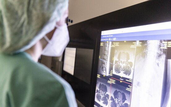 Medizinisches Fachpersonal mit Mundschutz analysiert MRT- und Röntgenbilder einer Wirbelsäule am Monitor