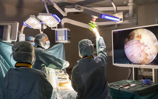 Chirurgenteam in OP-Kleidung operiert im modernen Operationssaal mit Monitoren und medizinischen Geräten