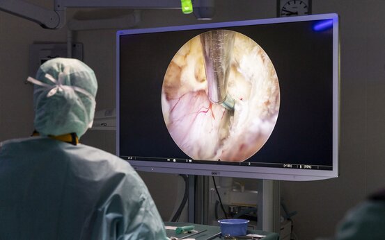 Chirurg in OP-Kleidung betrachtet während einer endoskopischen Operation einen Monitor mit Operationsfeld