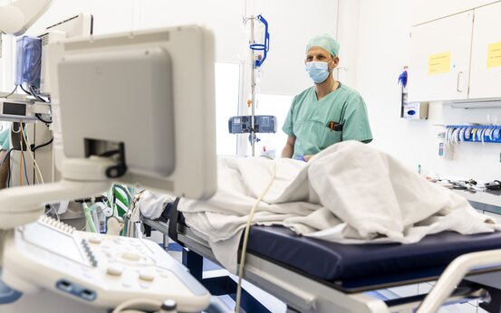 Arzt in grüner OP-Kleidung überwacht Patienten im Krankenhausbett mit moderner Medizintechnik