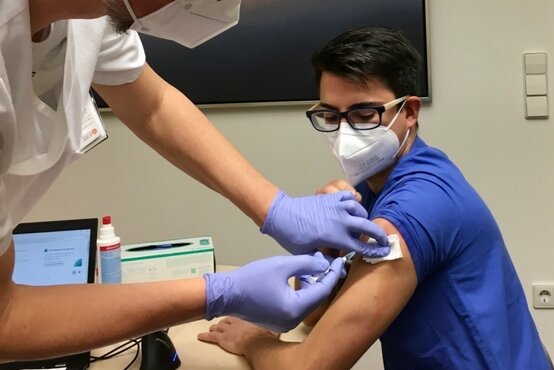 Zwei Personen mit FFP2-Masken, eine erhält eine Impfung in den Oberarm