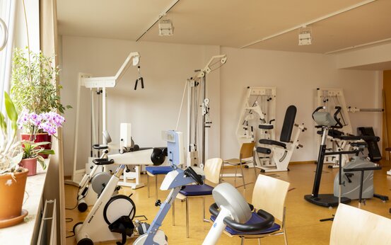 Heller Trainingsraum mit Fitness- und Rehabilitationsgeräten, großen Fenstern und Pflanzen