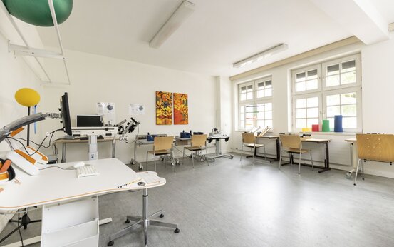Heller Therapieraum mit modernen Therapiegeräten, Tisch, Gymnastikbällen und Holzstühlen